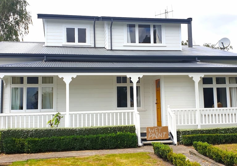 White weatherboard home with dark roof and porch detailing, freshly painted by Gee Cee Painters