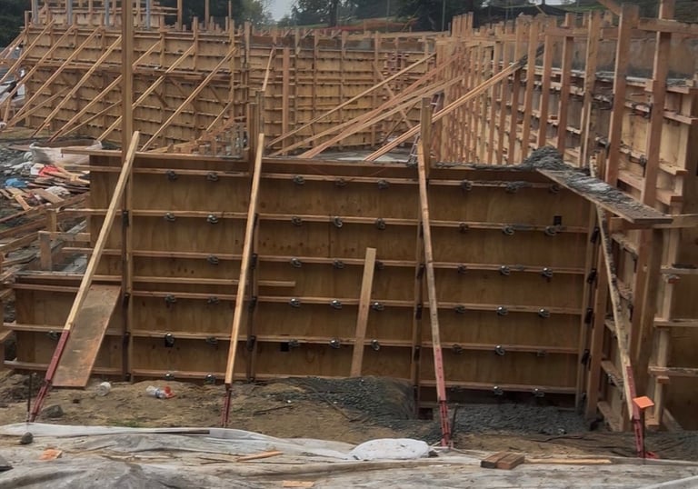 Wooden concrete formwork for a retaining wall foundation at a residential construction site.