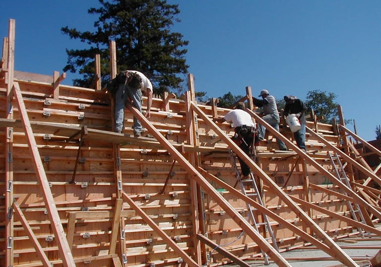 Construction crew assembling a wooden wall formwork system for a concrete foundation project.