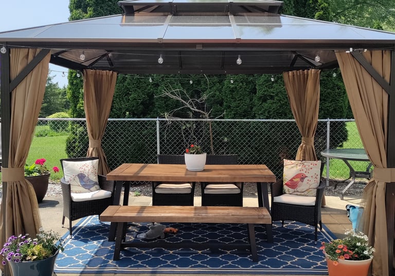 Hardtop backyard gazebo with outdoor dining table, benches, and privacy curtains on a patio rug.