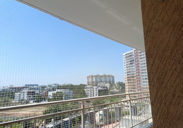 A bright balcony secured with a neatly installed white safety net overlooking a cityscape.