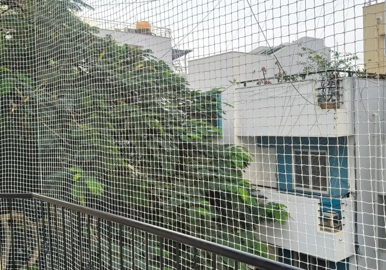 Wide shot of a residential balcony fully covered with a sturdy safety net, overlooking a quiet Sadas
