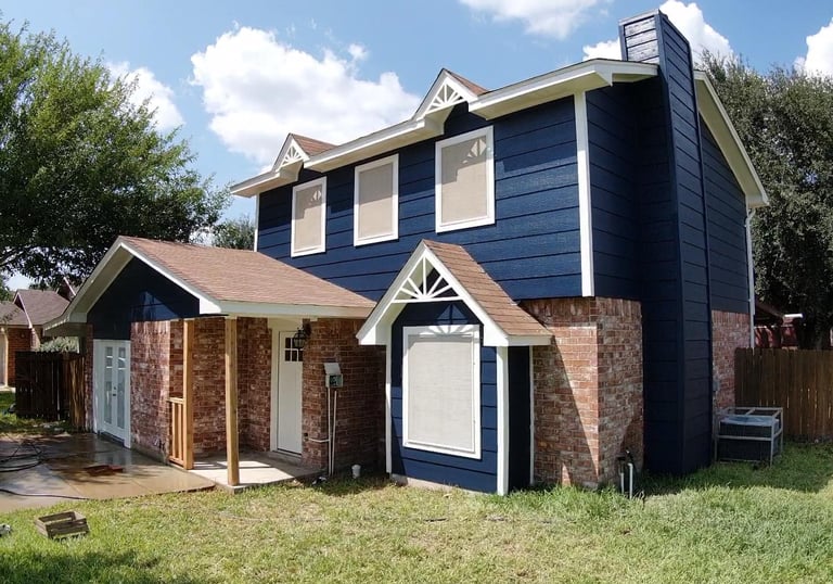 Two-story home with navy blue siding, white trim, and red brick exterior under a sunny sky.