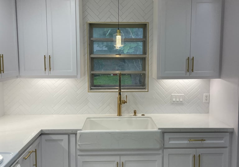 Modern white kitchen remodel with shaker cabinets, gold hardware, and a white farmhouse sink.