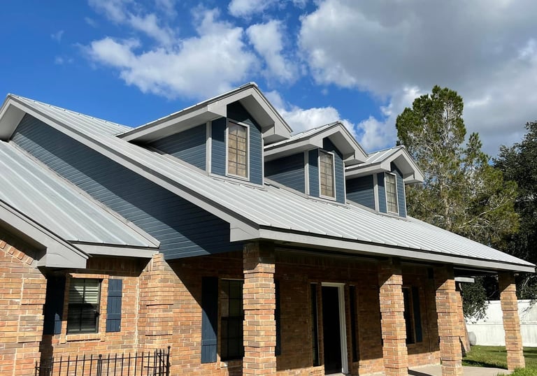 Modern suburban home with red brick exterior, blue siding, and a durable grey metal roof under a blue sky.