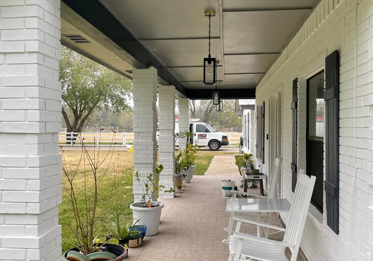 White rocking chairs on a covered ranch-style porch with white brick pillars and blue accents.
