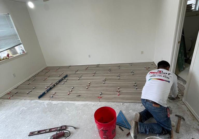 Professional contractor installing wood-look floor tiles using a leveling system in a residential room.