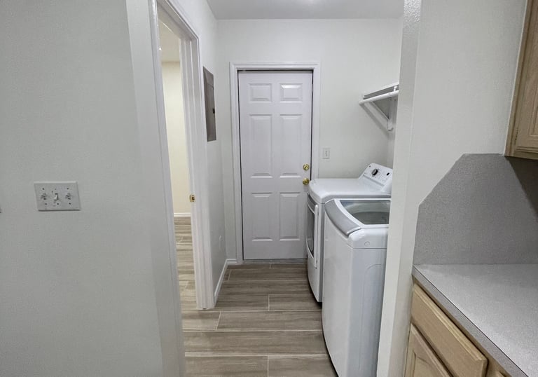 Modern laundry room with white top-load washer and dryer, wood-look tile flooring, and neutral walls.
