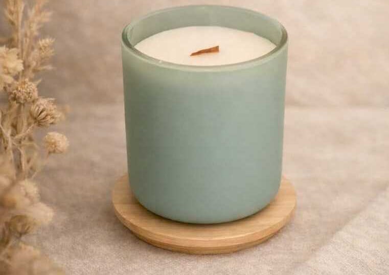 Vela de soja perfumada en un frasco de vidrio verde salvia mate con una mecha de madera sobre un pos