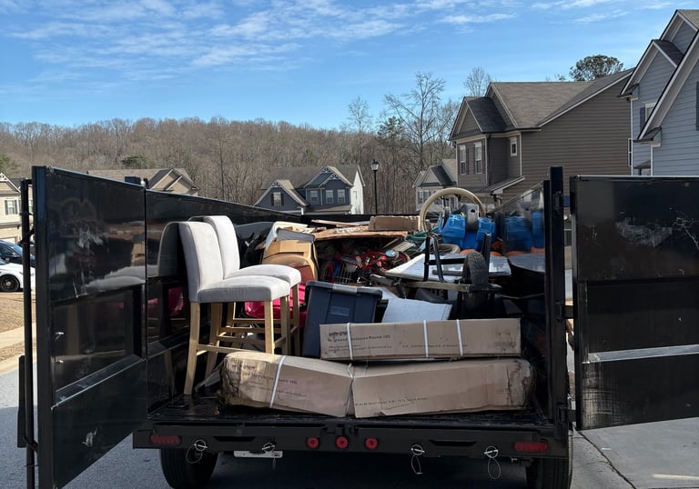 A junk removal trailer filled with furniture, boxes, and debris parked in a residential neighborhood.