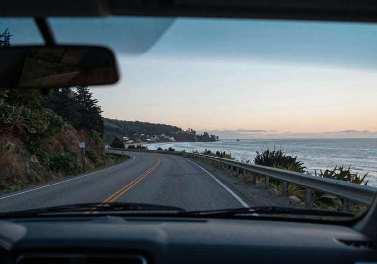 A view from inside a car through a perfectly clear, flawless windshield looking out at a scenic North American coastal road at dawn.