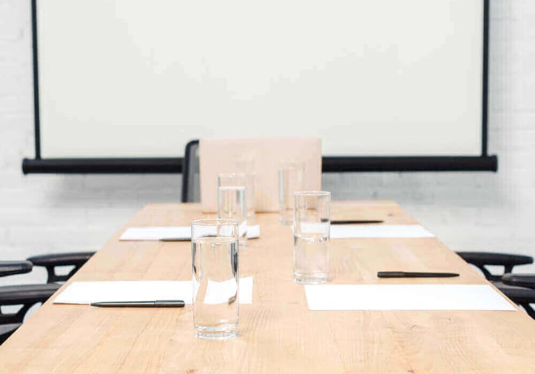 Empty corporate meeting room with water glasses, pens, and paper on a wooden table before a presentation.