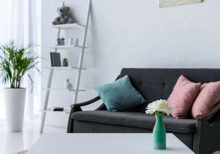 Modern living room with a white coffee table, grey sofa, and leaning ladder bookshelf decor.