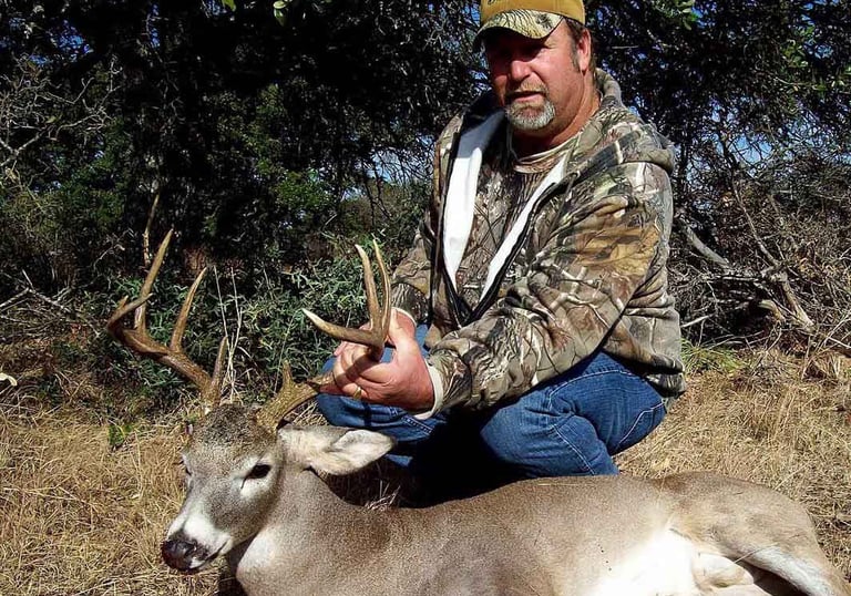 A successful hunter in camouflage posing with a harvested whitetail buck on a Mason County Texas ranch.