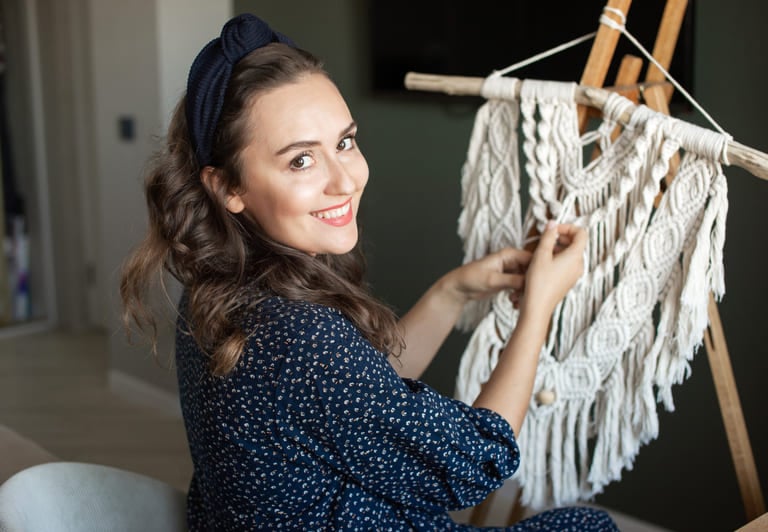 Mujer sonriente bordando un sueter con hilo de macramé