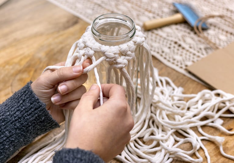 Manos bordando con hilos de macramé un jarrón de vidrio