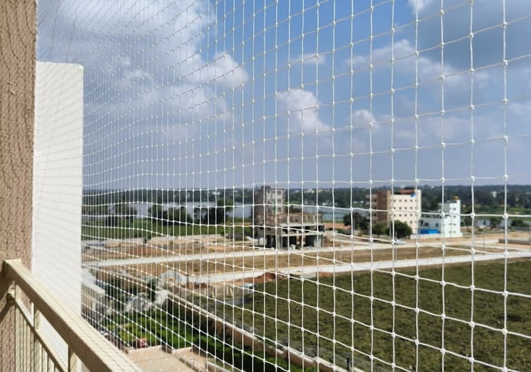 Wide-angle shot of a balcony fully covered with a safety net, sunlight casting shadows on the mesh i