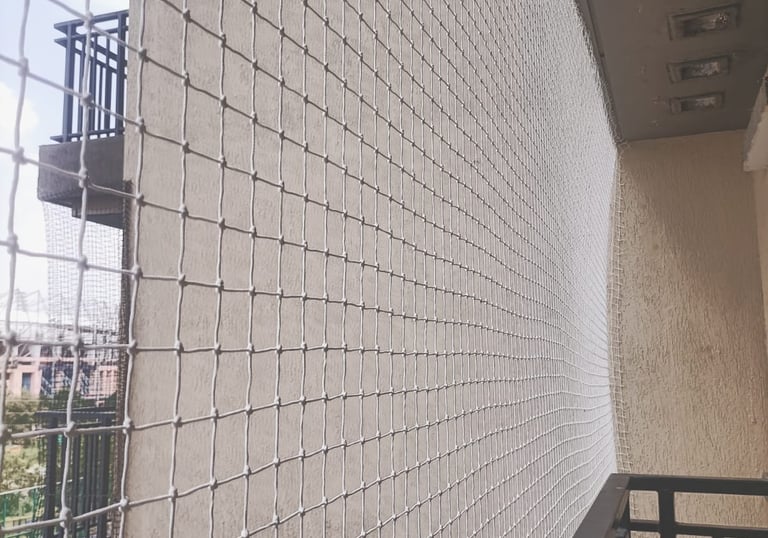 Installation process of anti-pigeon nets showing skilled hands securing the mesh tightly.