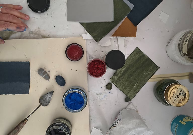 Overhead view of an artist workstation with pigment powders, paint swatches, and a palette knife.