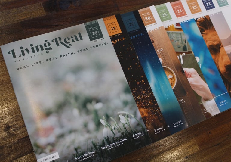 A collection of Living Real Magazine issues fanned out on a wooden table, showcasing faith-based lifestyle content.