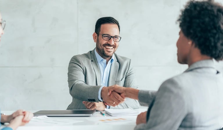 A smiling loan officer in a grey suit shaking hands during a successful loan closing.
