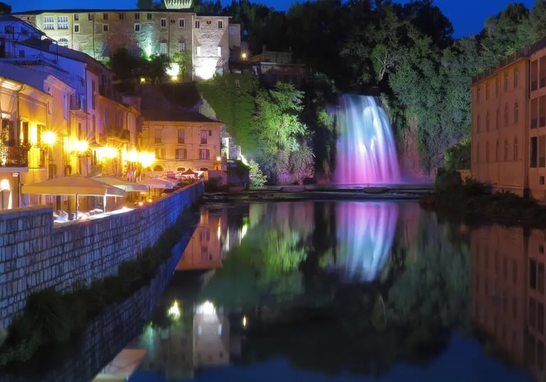The Great Waterfall of Isola del Liri illuminated at night with colorful lights reflecting on the river