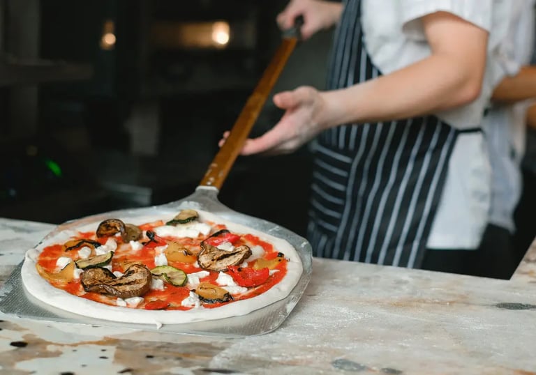Chef sliding fresh Italian pizza into a wood-fired oven in a traditional pizzeria