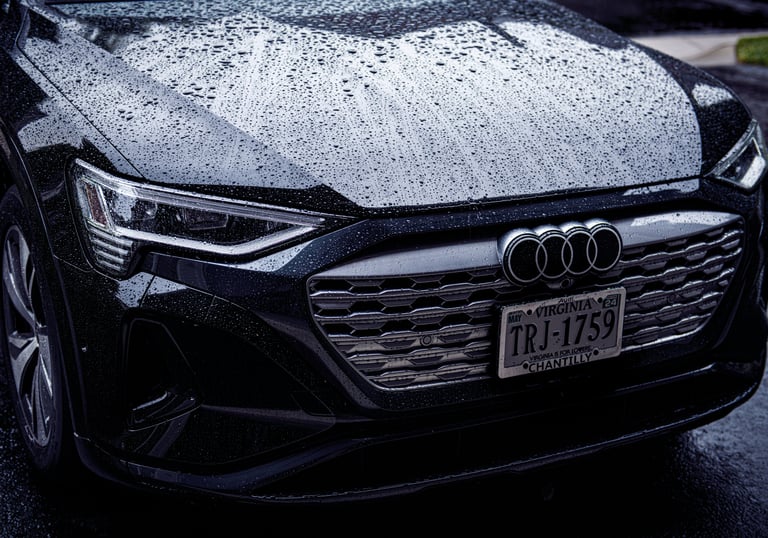 Front view of a black Audi electric vehicle covered in rain droplets with visible headlights and grille.