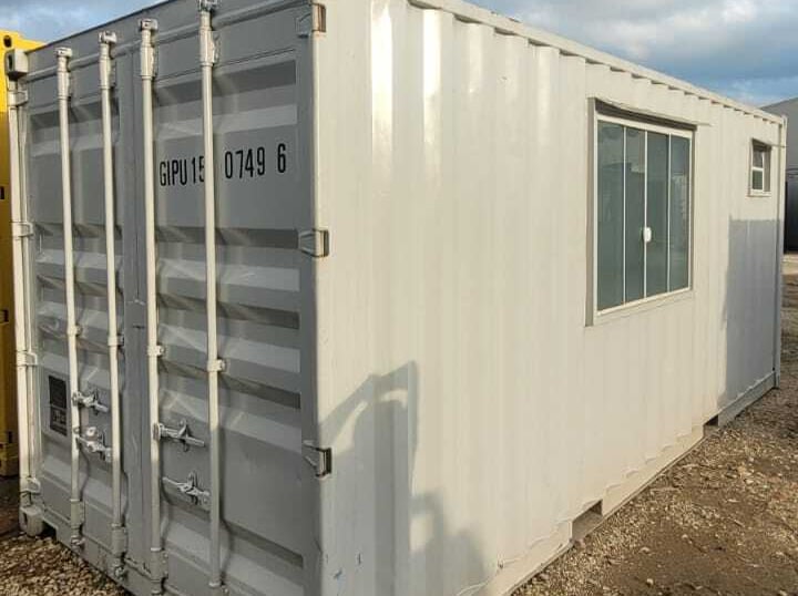 container para obra na cor cinza com uma janela em uma paisagem no patio de um estacionamento