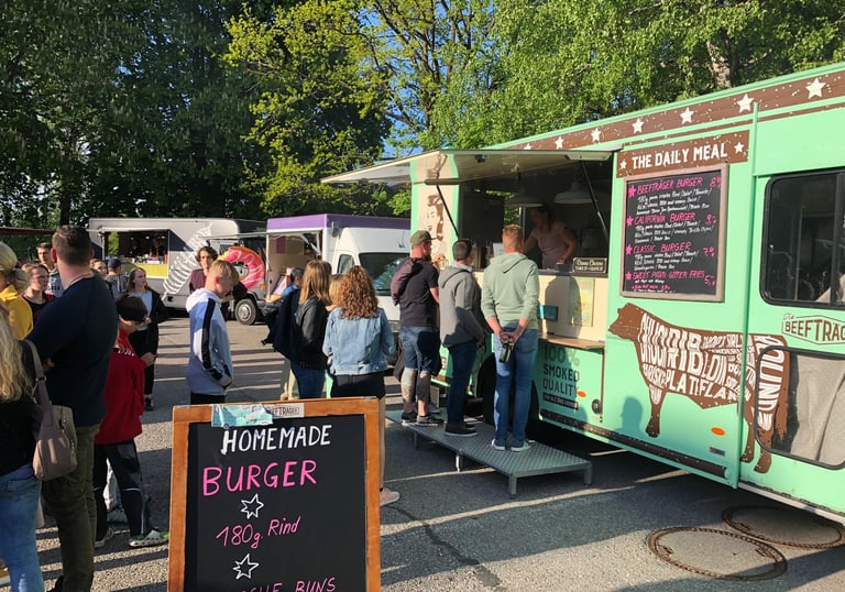 Customers lining up at a green gourmet food truck serving homemade burgers on brioche buns.