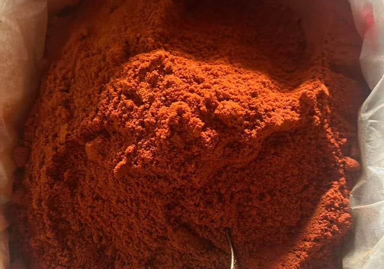Close-up of vibrant red chili powder inside a large bag with a metal measuring scoop.