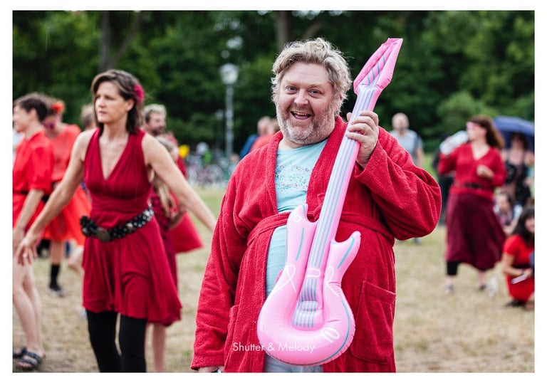 Ein lächelnder Mann im Bademantel mit einer rosa aufblasbaren Gitarre.