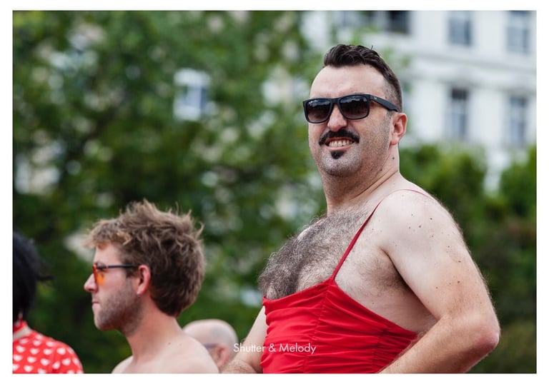 Ein Mann mittleren Alters mit behaarter Brust, rotem Kleid und Sonnenbrille.