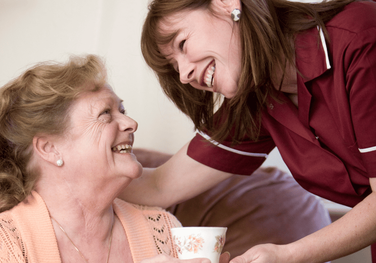 Image of an AMG Nursing & Care Services nurse smiling and proving a cup of tea to a patient in her home
