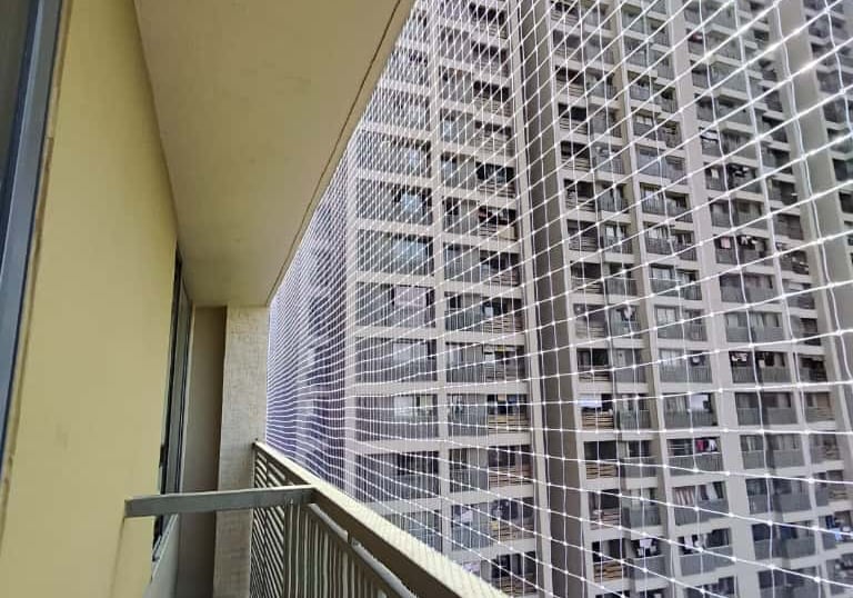 A wide shot of a high-rise balcony fitted with a durable pigeon-proof safety net under bright daylig