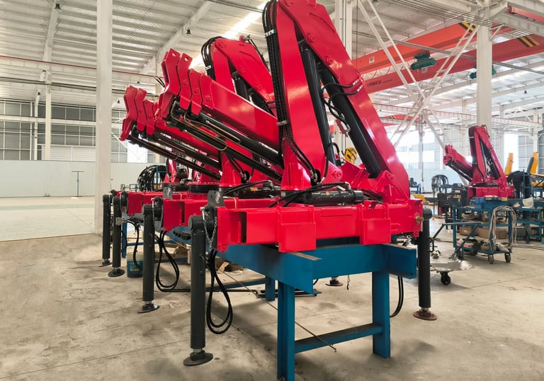 Production line: Red SQZ68B.3 (3.2T) articulating knuckle boom cranes on blue stands, pre-vehicle mounting.