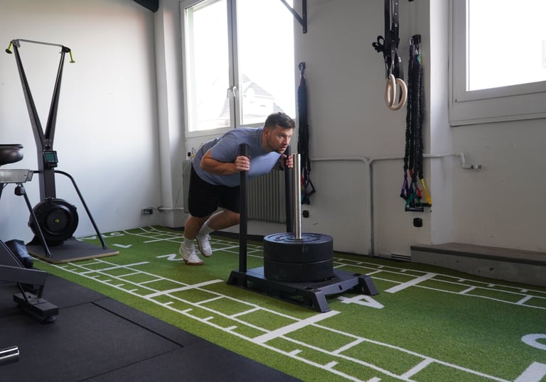 in Mann beim intensiven Training mit dem Gewichtsschlitten (Sled Push) auf grünem Kunstrasen