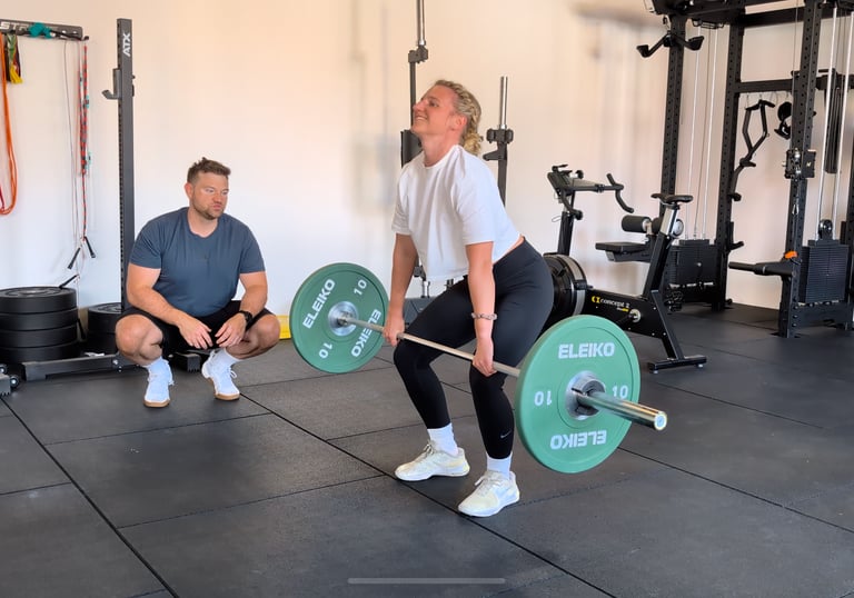 Eine Frau beim Kreuzheben mit Langhantel unter Anleitung eines Personal Trainers in einem Bielefeld