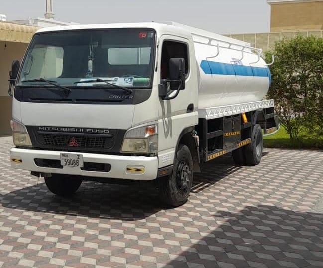 a truck with a tanker truck parked in front of a building