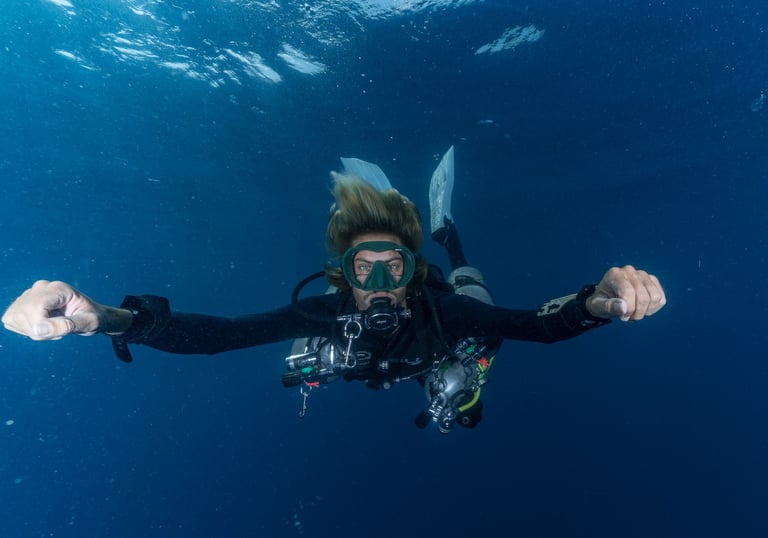 A scuba diver in full gear glides through clear blue ocean water during a deep sea dive.