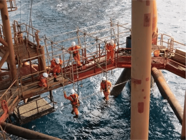 Offshore oil rig workers performing maintenance on scaffolding over the ocean.
