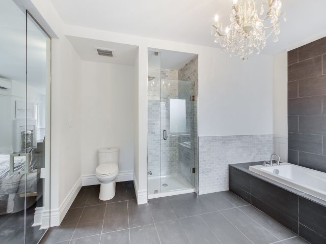 a large master bathroom with a toilet, shower stall, and soaker tub tiled in black