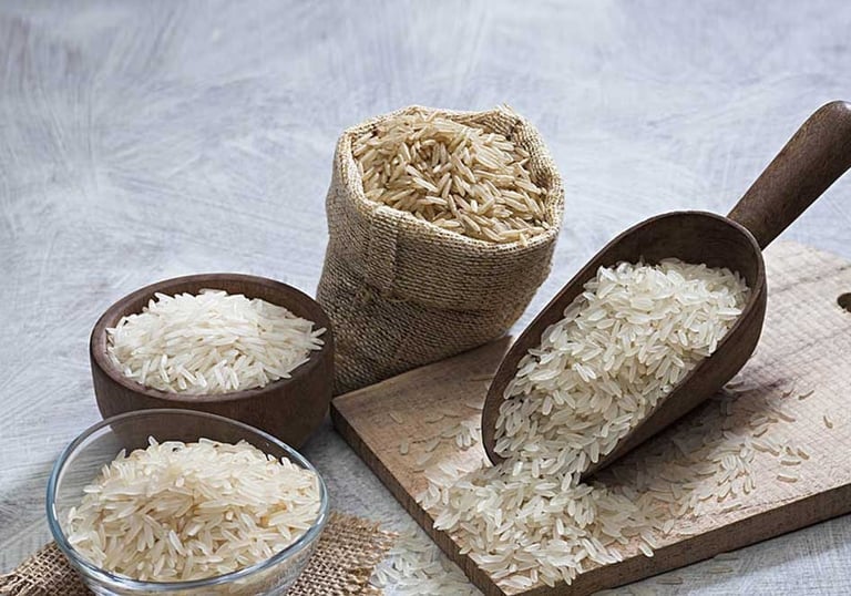 variety of rice types in jute sack and wooden scoops on a white baground
