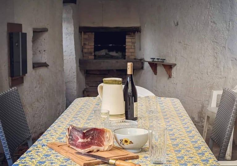 Une table sur la terrasse avec un morceau de jambon, une carafe et une bouteille de vin posée dessus