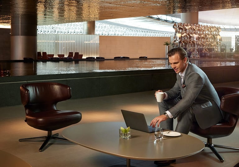 Man in suit working on laptop next to reflection pool in Qatar Airways Al Mourjan Lounge