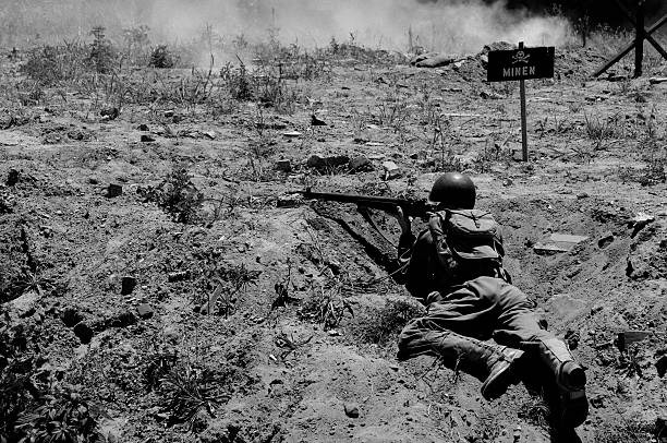 World War II soldier aiming a rifle from a trench near a German minefield warning sign.