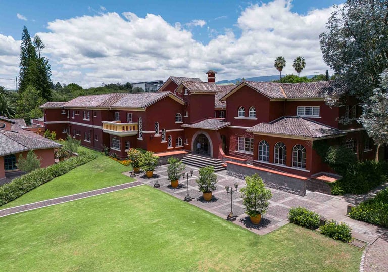 Fotografía aérea de gran casa religiosa de color rojo rodeada de hermoso jardín verde en Quito Ecuador
