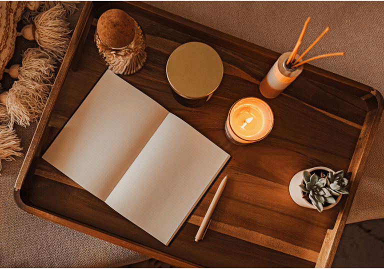 A wooden tray with an open notebook, pen, scented candle, and succulent for a cozy journaling setup.