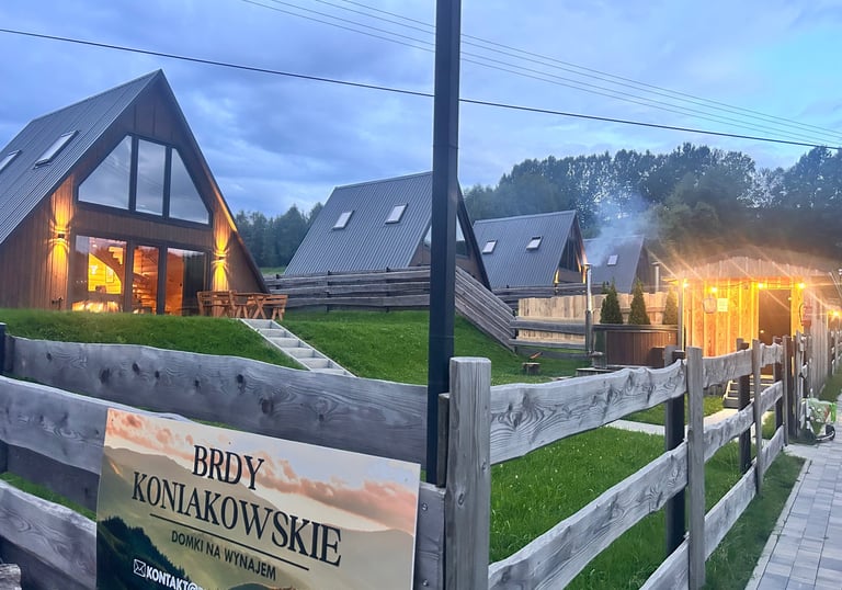 Modern A-frame wooden cabins at Brdy Koniakowskie resort with evening lighting and mountain views.