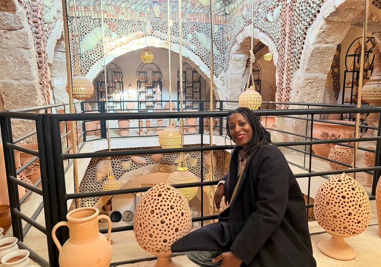A woman inside a shop in Tunisia sitting on a balcony with vases around and mosaic tiles walls